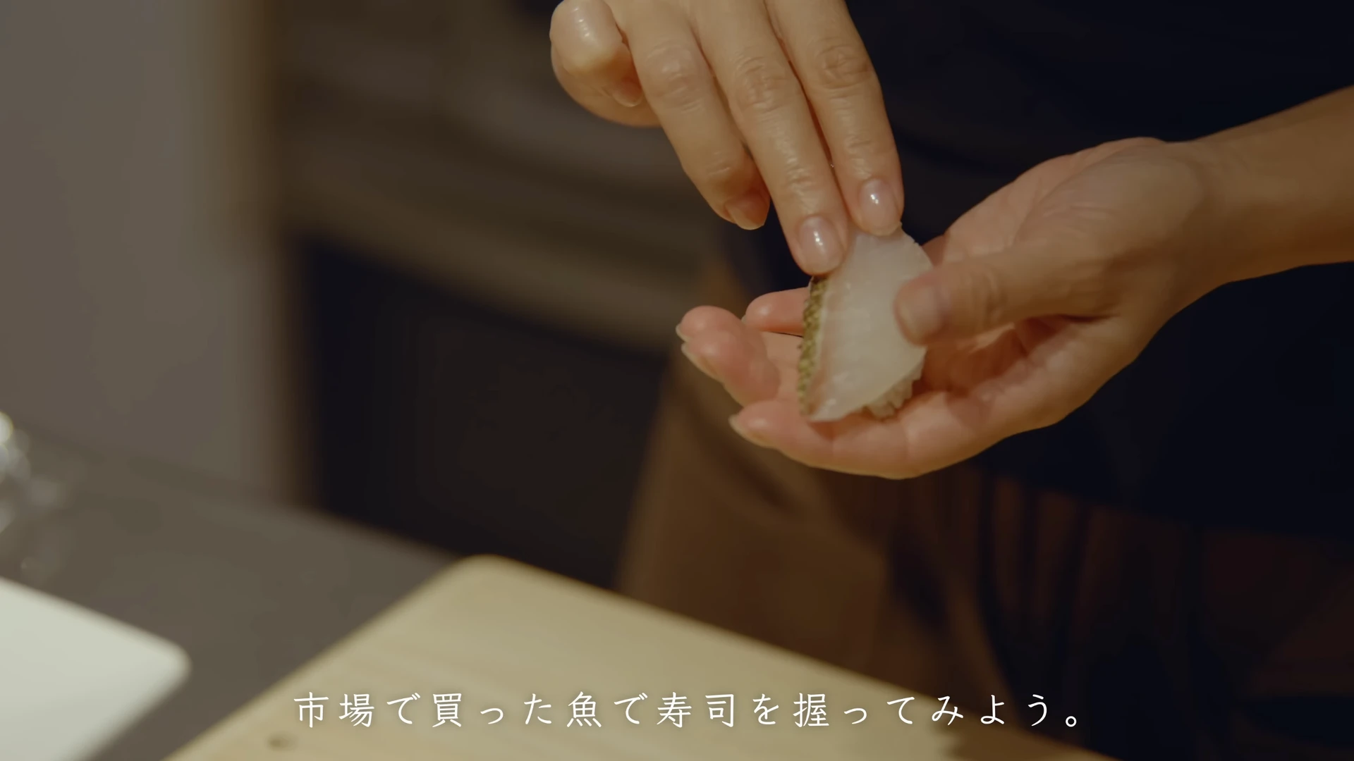 魚の切り身をのせて寿司を握る手元。「市場で買った魚で寿司を握ってみよう。」の字幕